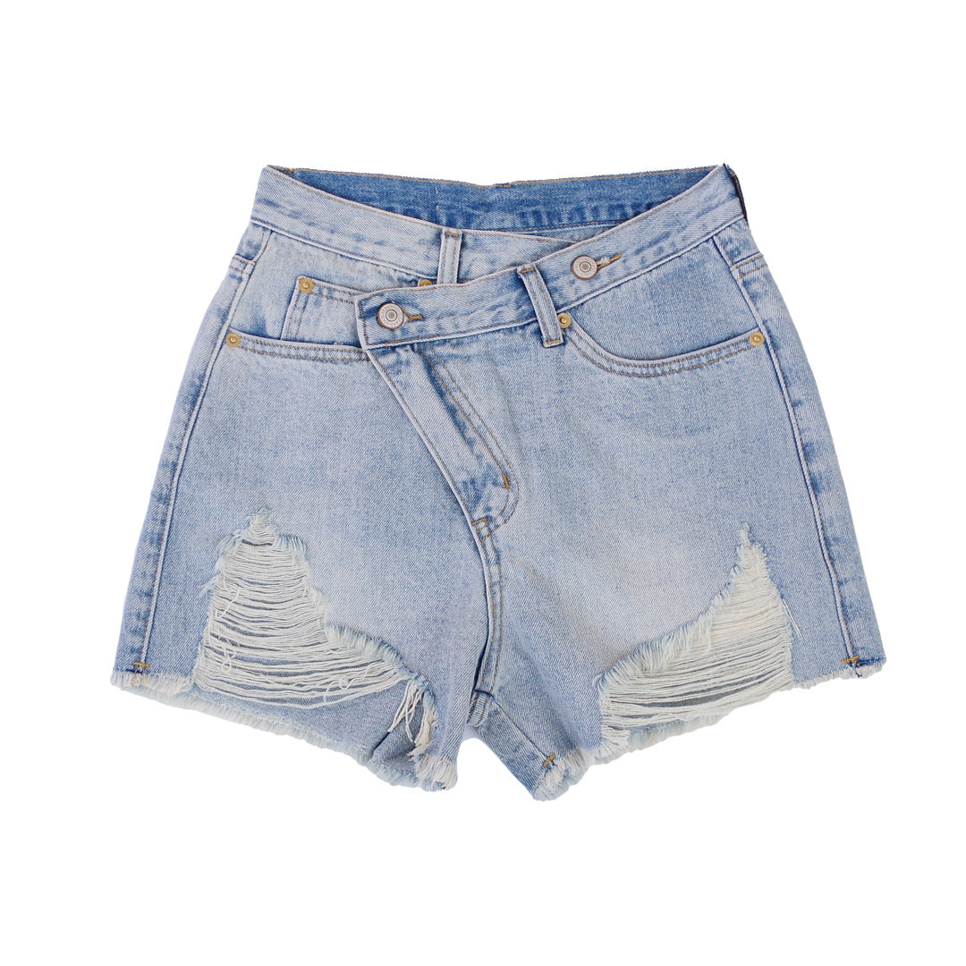 Woman wearing light wash denim shorts with asymmetrical waist and distressed hem.