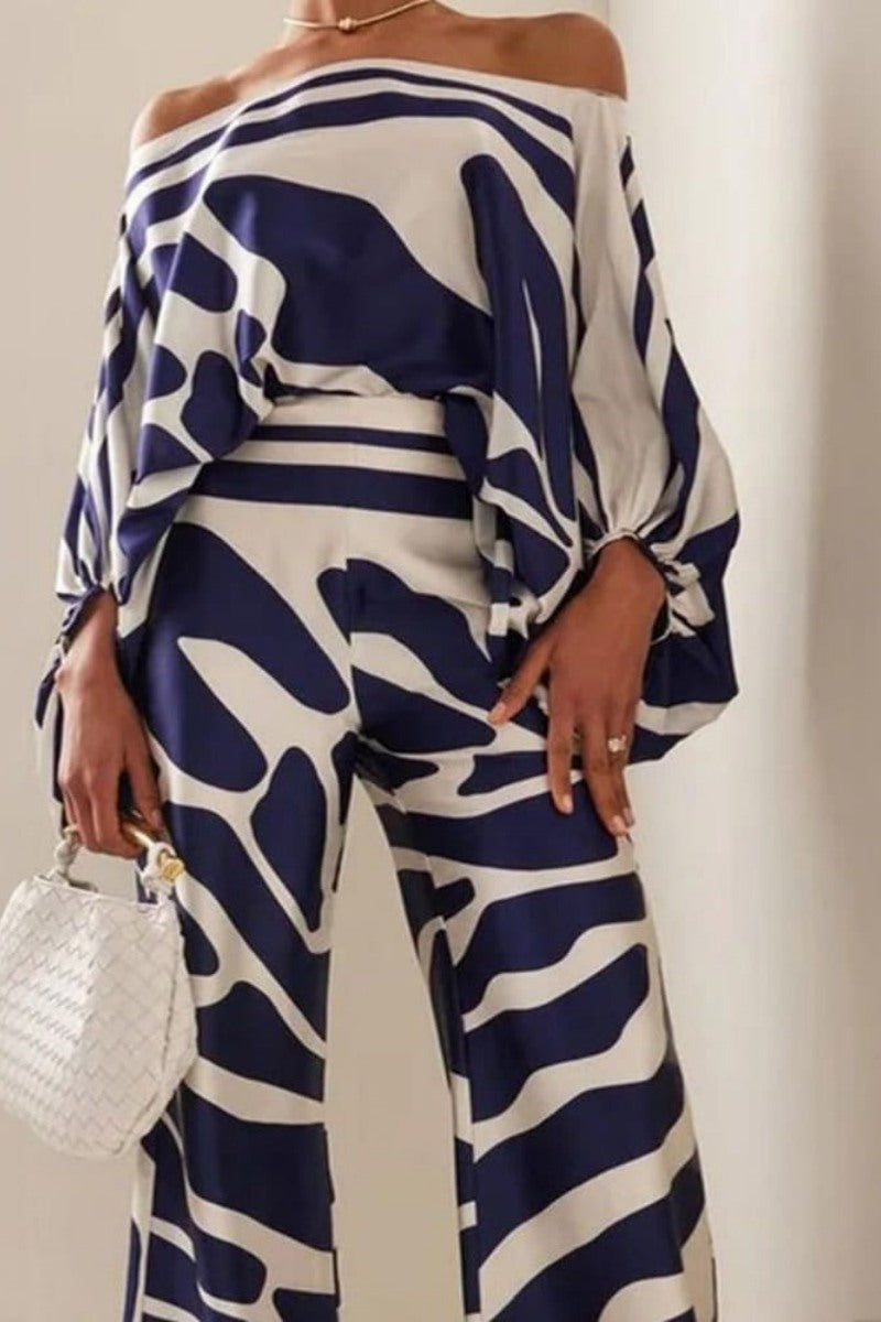 Woman wearing navy and ivory patterned satin two-piece set with off-the-shoulder top and wide-leg pants.