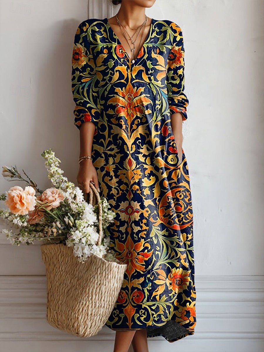 4XL - A woman wearing a long-sleeved, V-neck maxi dress featuring a vibrant blue, orange, and yellow Art Nouveau botanical print, holding a straw basket filled with flowers.