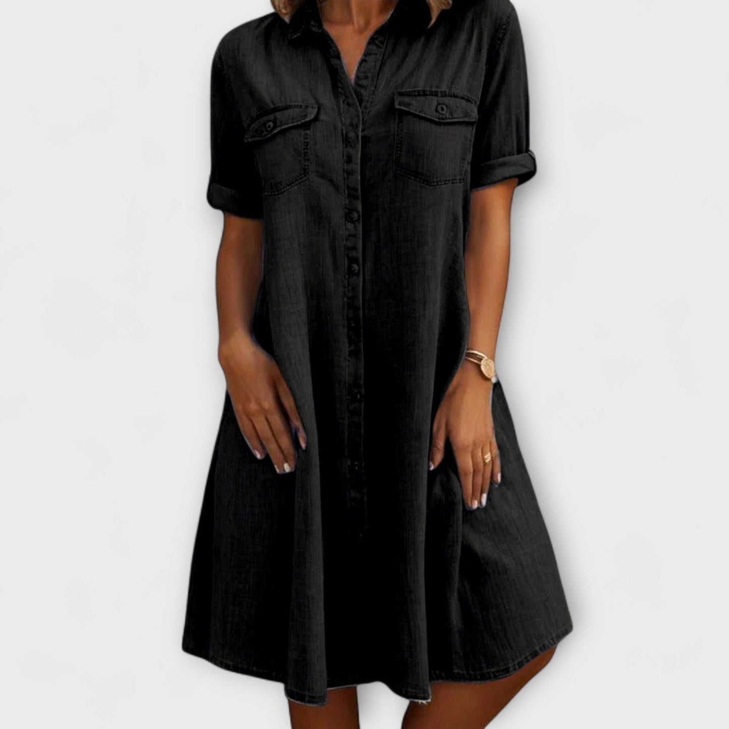 Black - A woman wearing a light blue chambray short-sleeve button-down sundress with chest pockets and a relaxed fit.