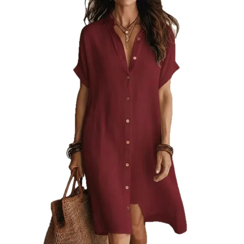 Burgundy - A woman wearing a black, short-sleeved linen midi shirt dress with a button-down front, styled with a woven straw tote bag.