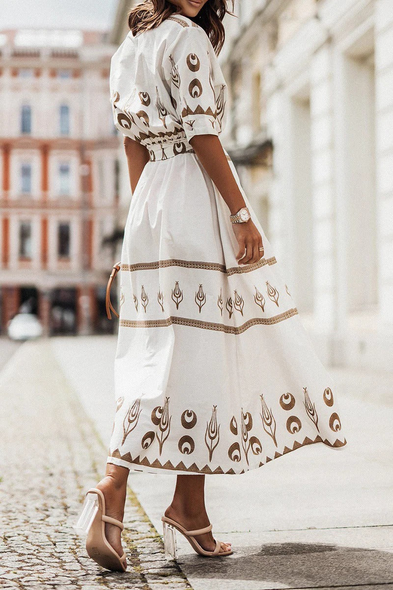 White - A woman wearing a black midi-length shirt dress with a gold geometric border print, featuring a collared neckline, short sleeves, a belted waist, and an A-line skirt.
