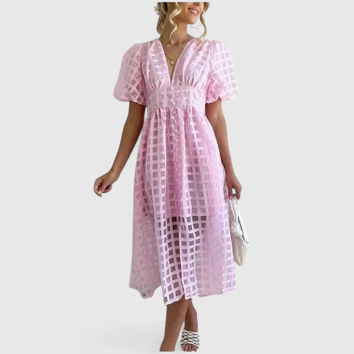 Baby Pink - A woman wearing a black grid organza midi dress with puff sleeves, a deep V-neck, and a button-front bodice, holding a woven beige handbag.