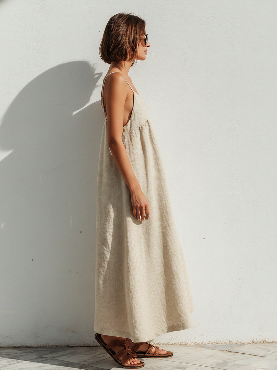 Beige - Model wearing an oversized woven maxi dress with spaghetti straps, a V-neckline, and side pockets, standing outdoors in bright sunlight.