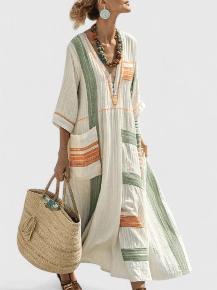 Beige 5 - Woman walking wearing a long, oversized striped maxi dress with half sleeves, front patch pockets, and side slits, carrying a woven tote bag.