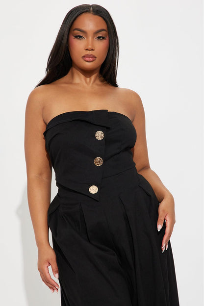 Woman in black one-shoulder woven jumpsuit with gold buttons