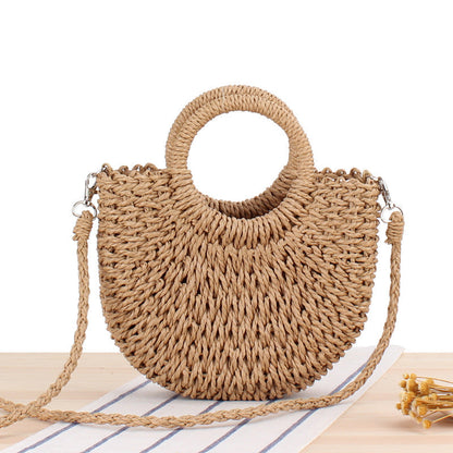 Front view of tan woven straw half-moon bag with round handle and braided shoulder strap
