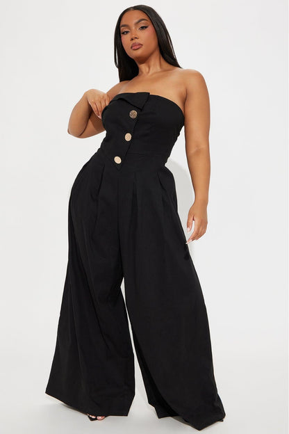 Woman in black one-shoulder woven jumpsuit with gold buttons