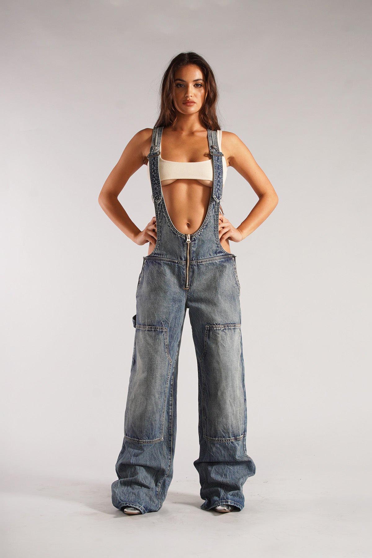 Woman wearing olive green cotton canvas overalls with cutout sides and white crop top