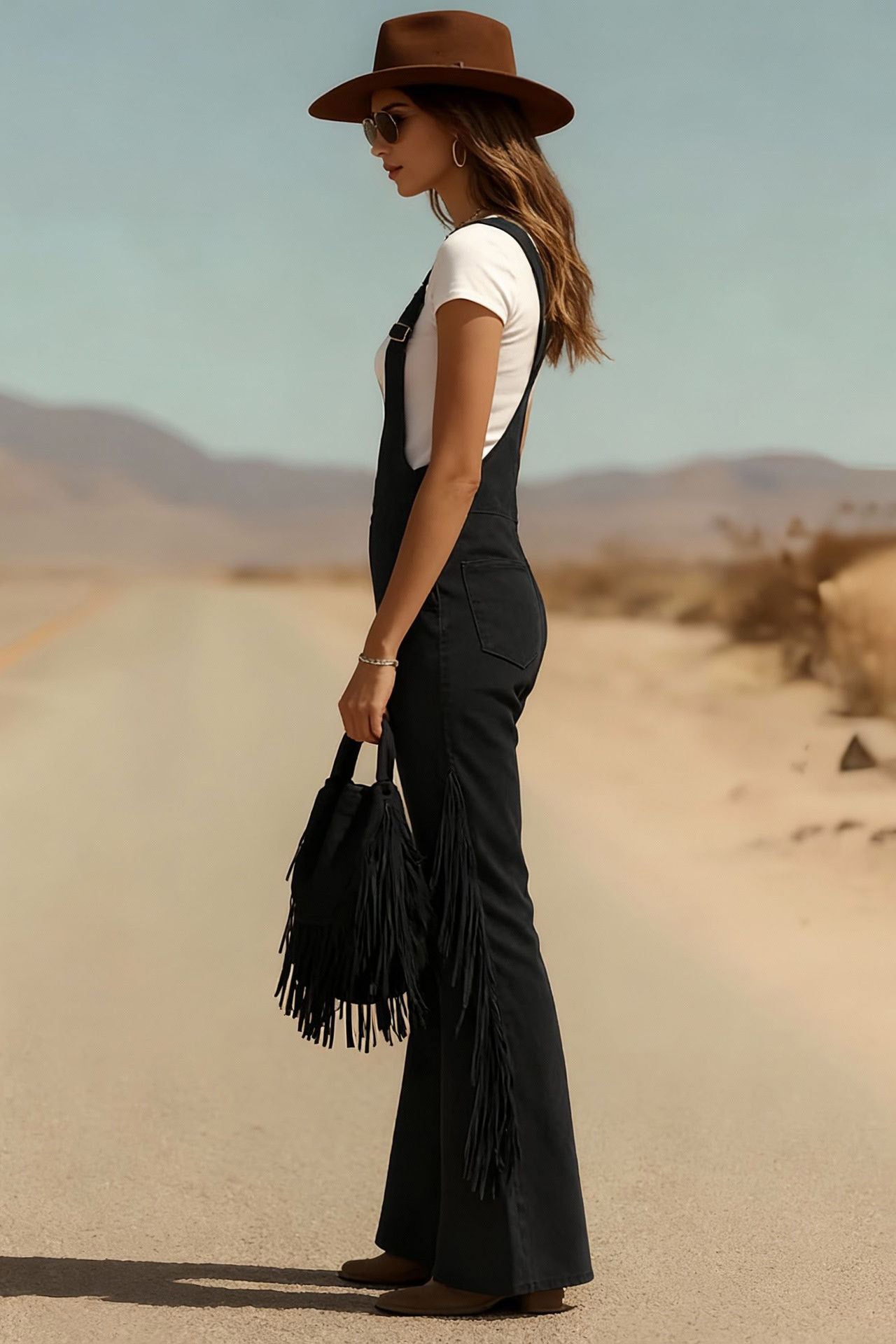 Woman in brown suede fringe overalls and hat walking in desert landscape