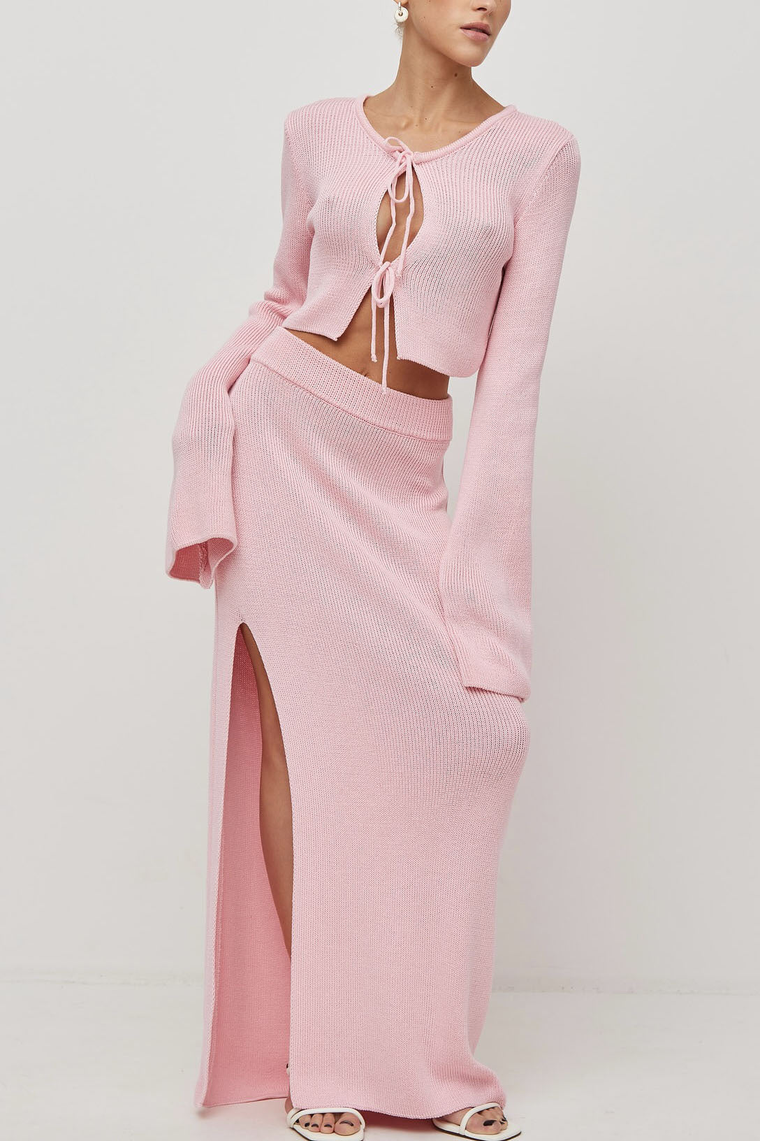 Woman wearing pink ribbed knit cardigan and skirt set with high slit.