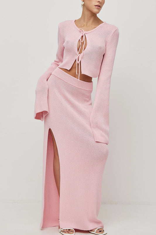 Woman wearing pink ribbed knit cardigan and skirt set with high slit.
