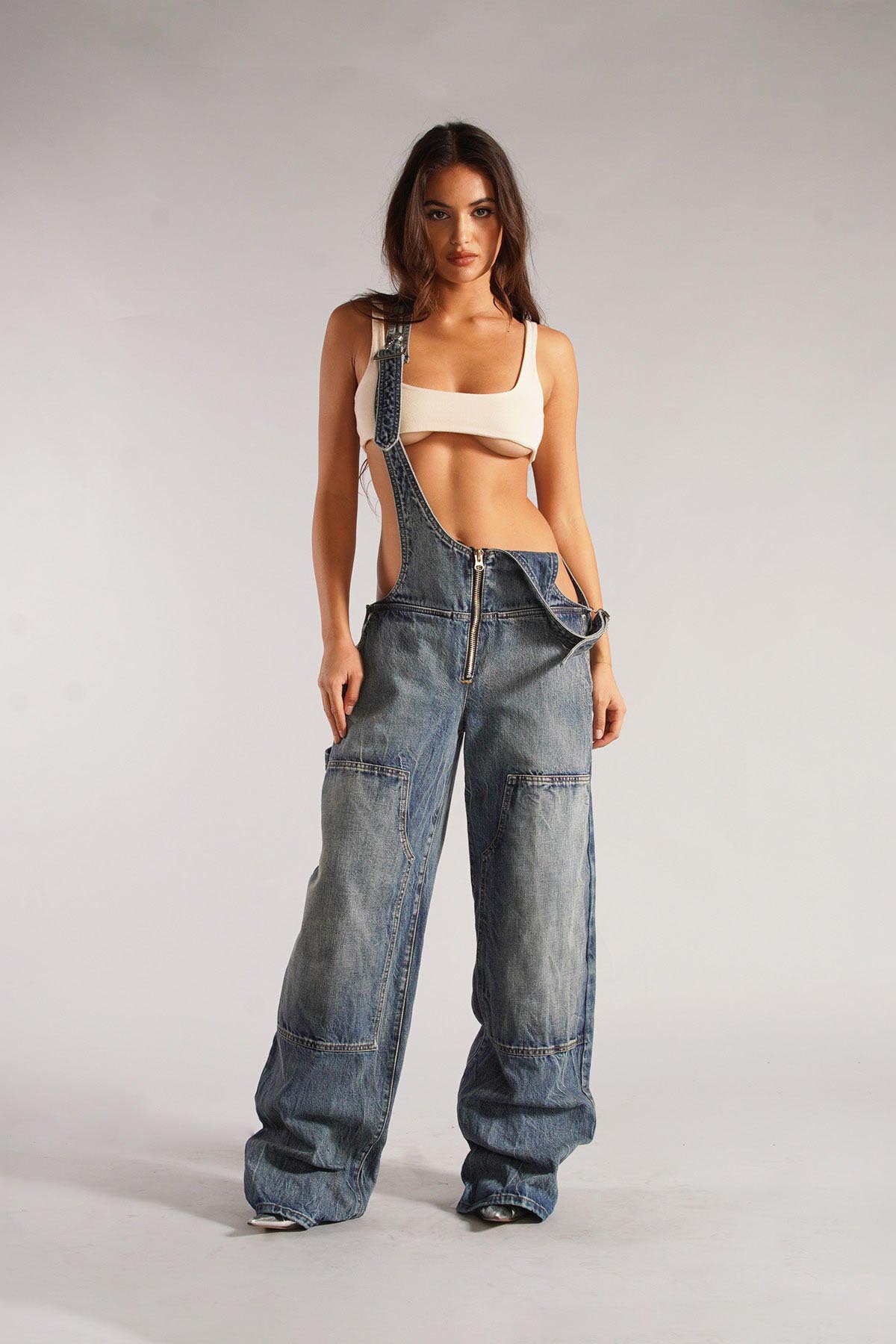 Woman wearing olive green cotton canvas overalls with cutout sides and white crop top