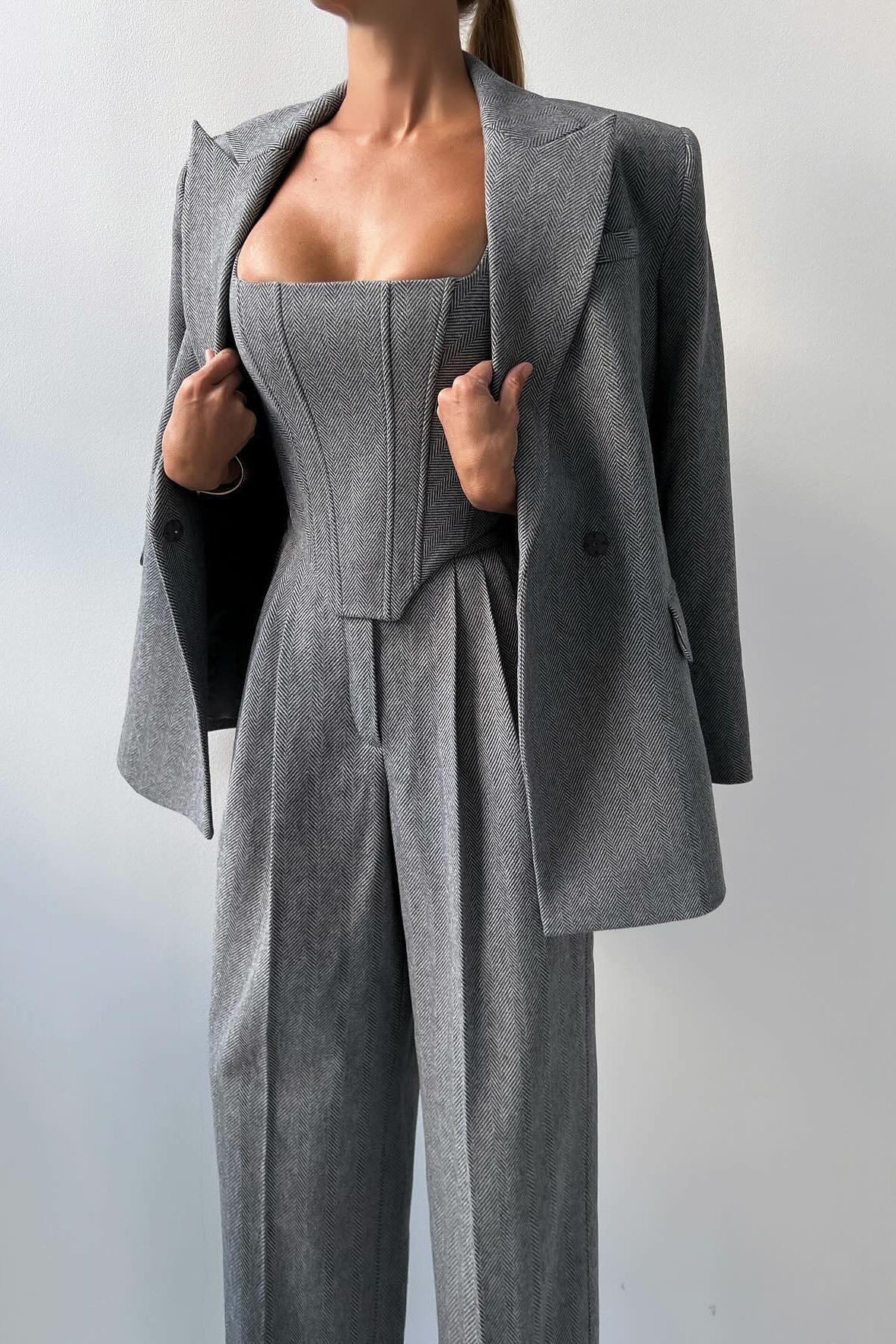 Woman in gray herringbone corset top, wide leg pants, and blazer