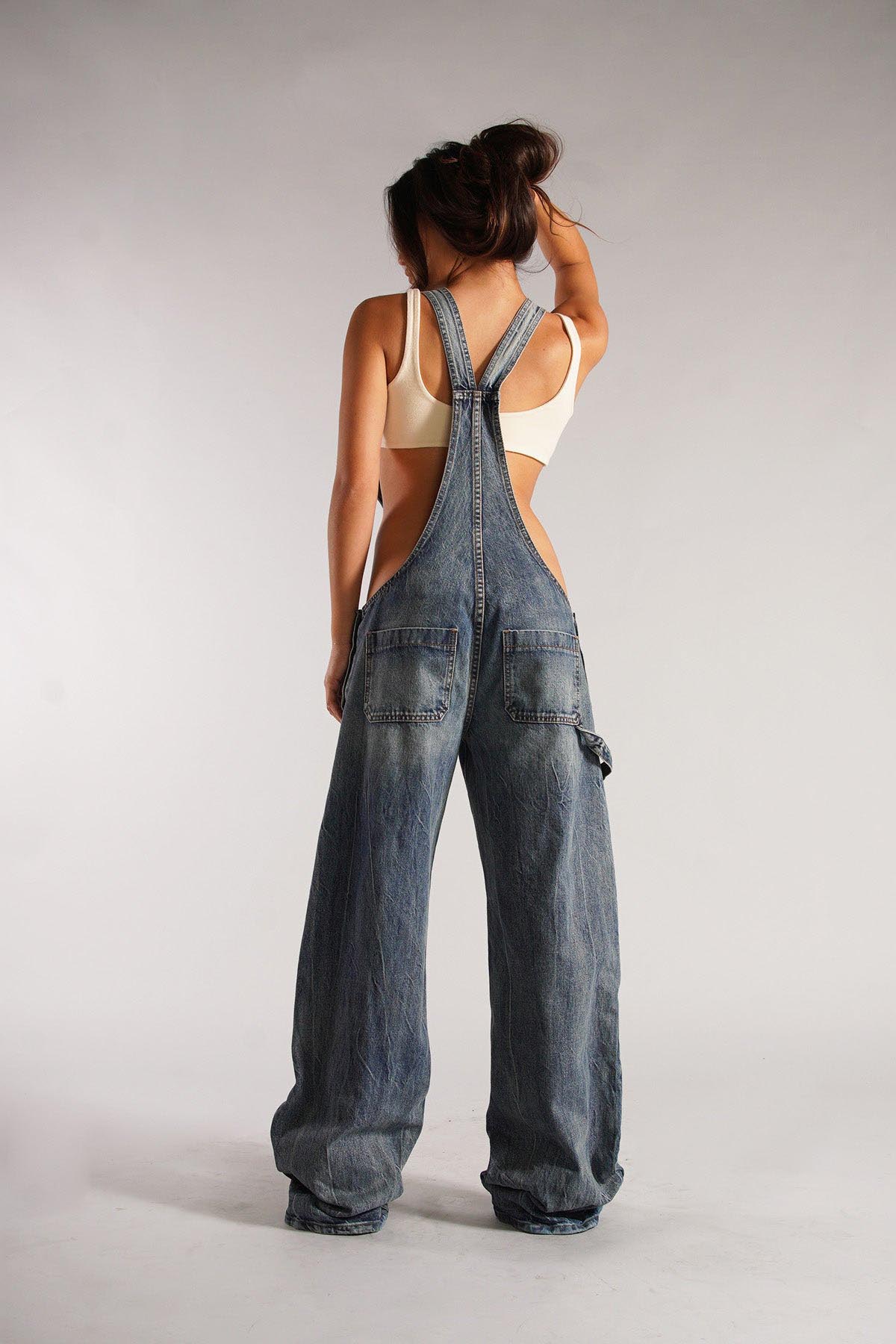 Woman wearing olive green cotton canvas overalls with cutout sides and white crop top