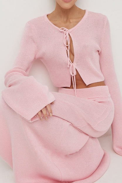 Woman wearing pink ribbed knit cardigan and skirt set with high slit.