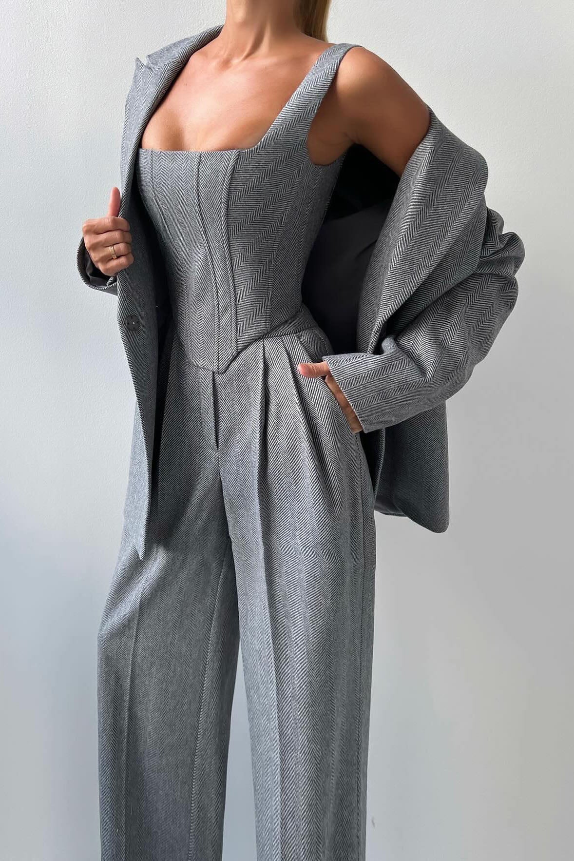 Woman in gray herringbone corset top, wide leg pants, and blazer