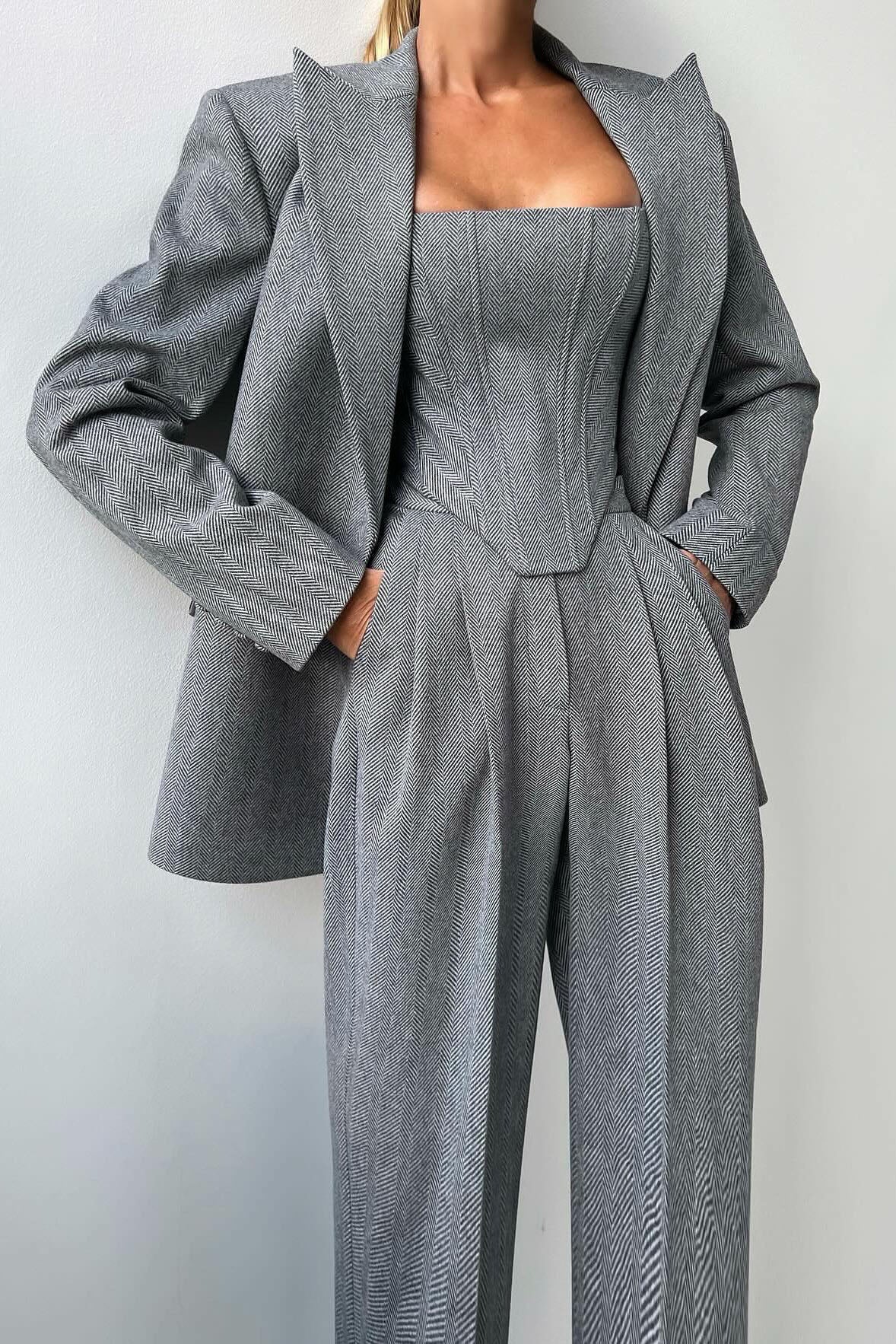 Woman in gray herringbone corset top, wide leg pants, and blazer