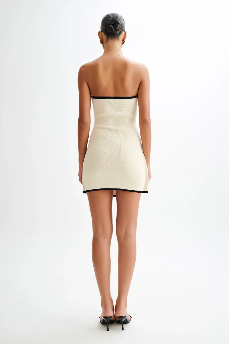 Woman wearing ivory ribbed knit strapless mini dress with black trim and tie waist.