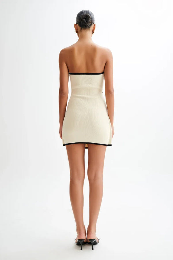 Woman wearing ivory ribbed knit strapless mini dress with black trim and tie waist.