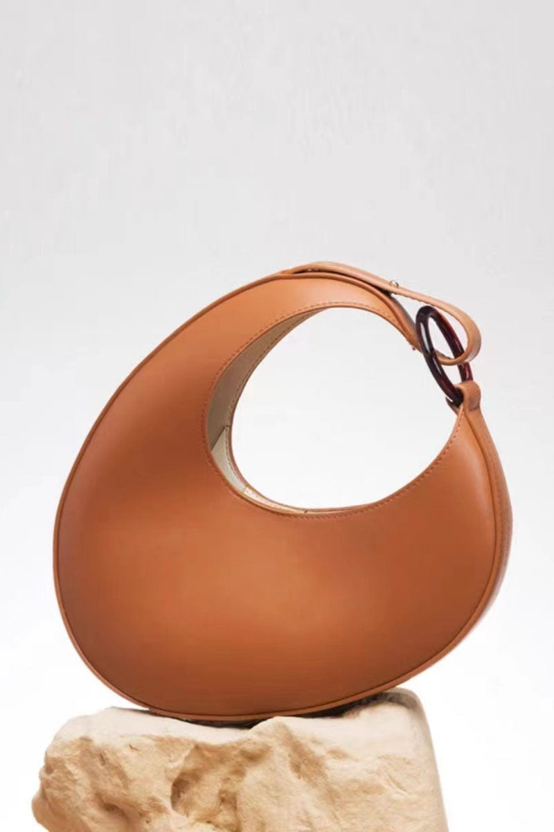 Tan leather half moon bag with resin handle detail on a stone surface