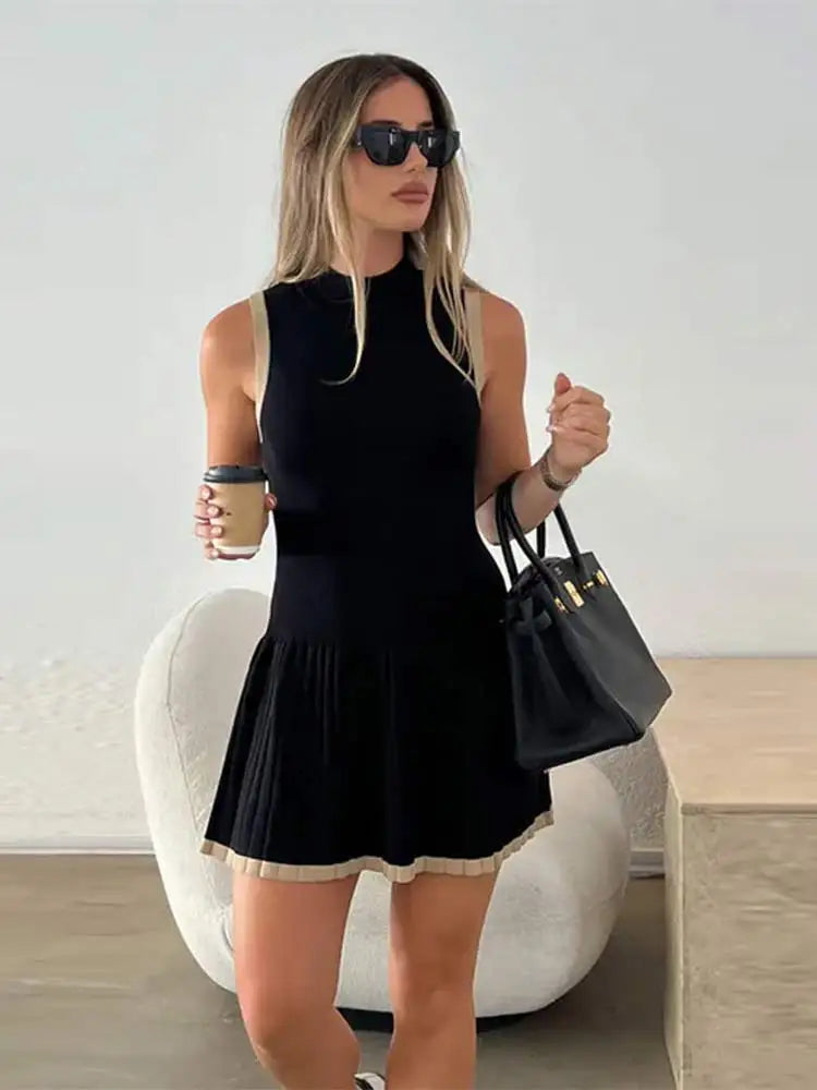Woman in black ribbed knit mini dress with tan trim, holding coffee and purse.