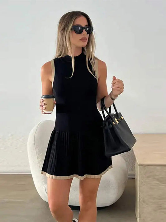 Woman in black ribbed knit mini dress with tan trim, holding coffee and purse.