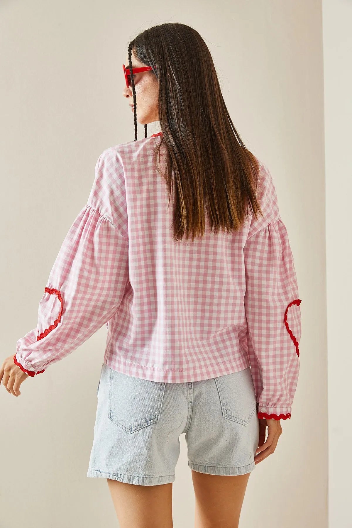 Woman in pink gingham blouse with heart pockets and denim shorts