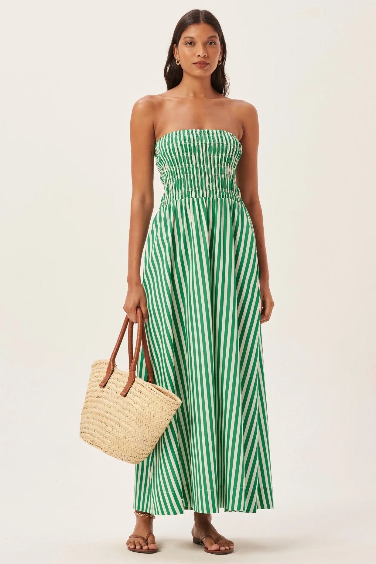 Woman in green and white striped strapless maxi dress holding straw tote bag