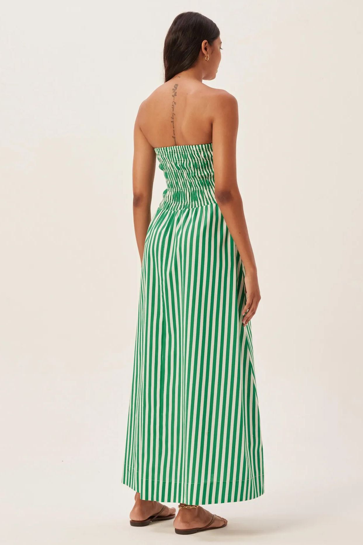 Woman in green and white striped strapless maxi dress holding straw tote bag