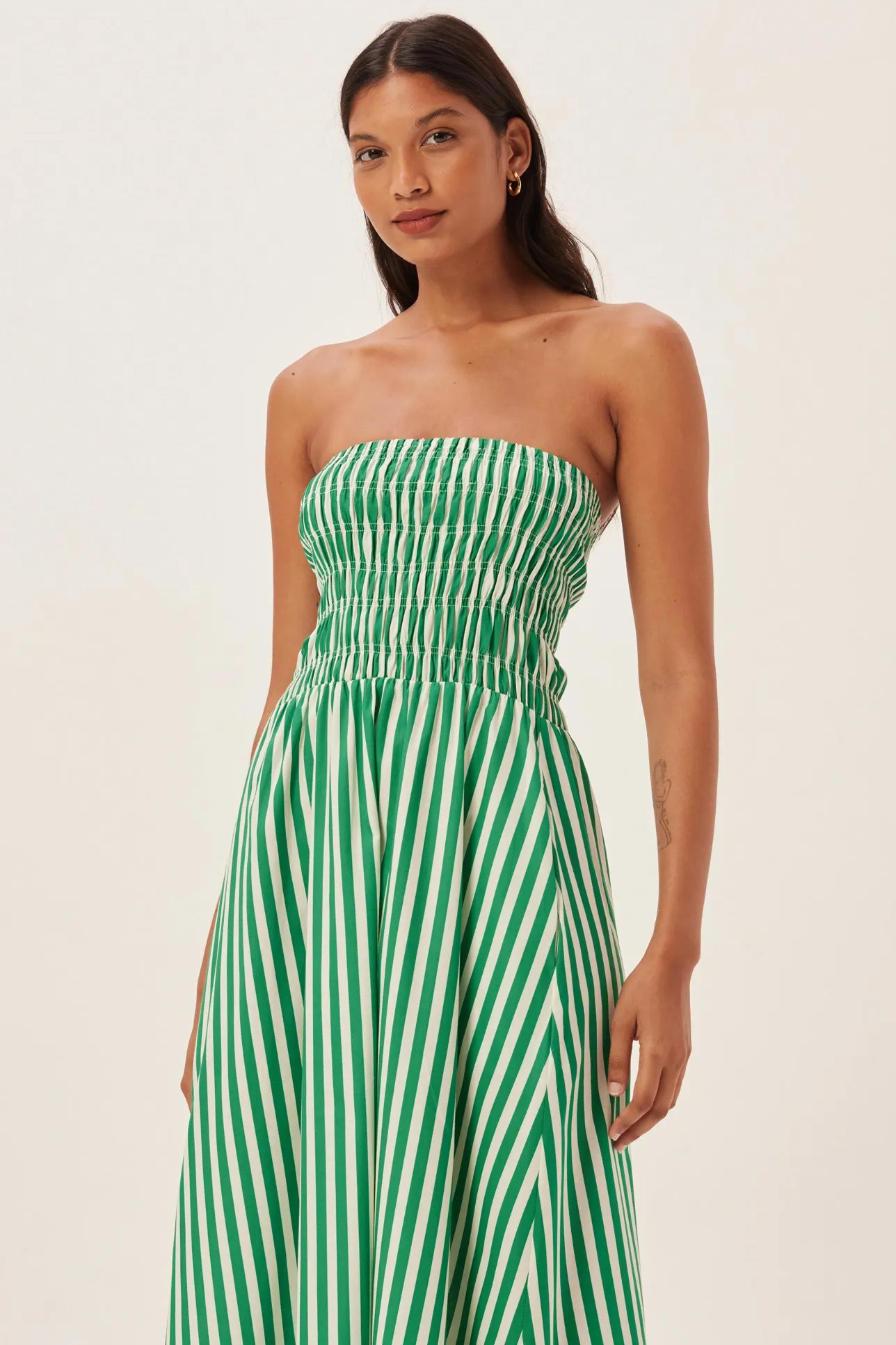 Woman in green and white striped strapless maxi dress holding straw tote bag