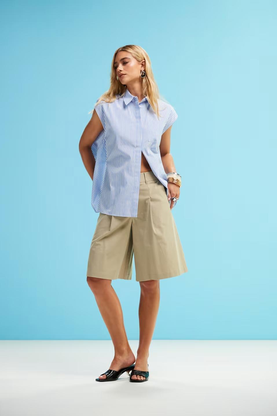 Woman in blue and white striped sleeveless shirt and khaki shorts holding a straw bag