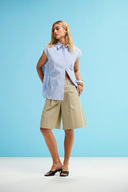 Woman in blue and white striped sleeveless shirt and khaki shorts holding a straw bag