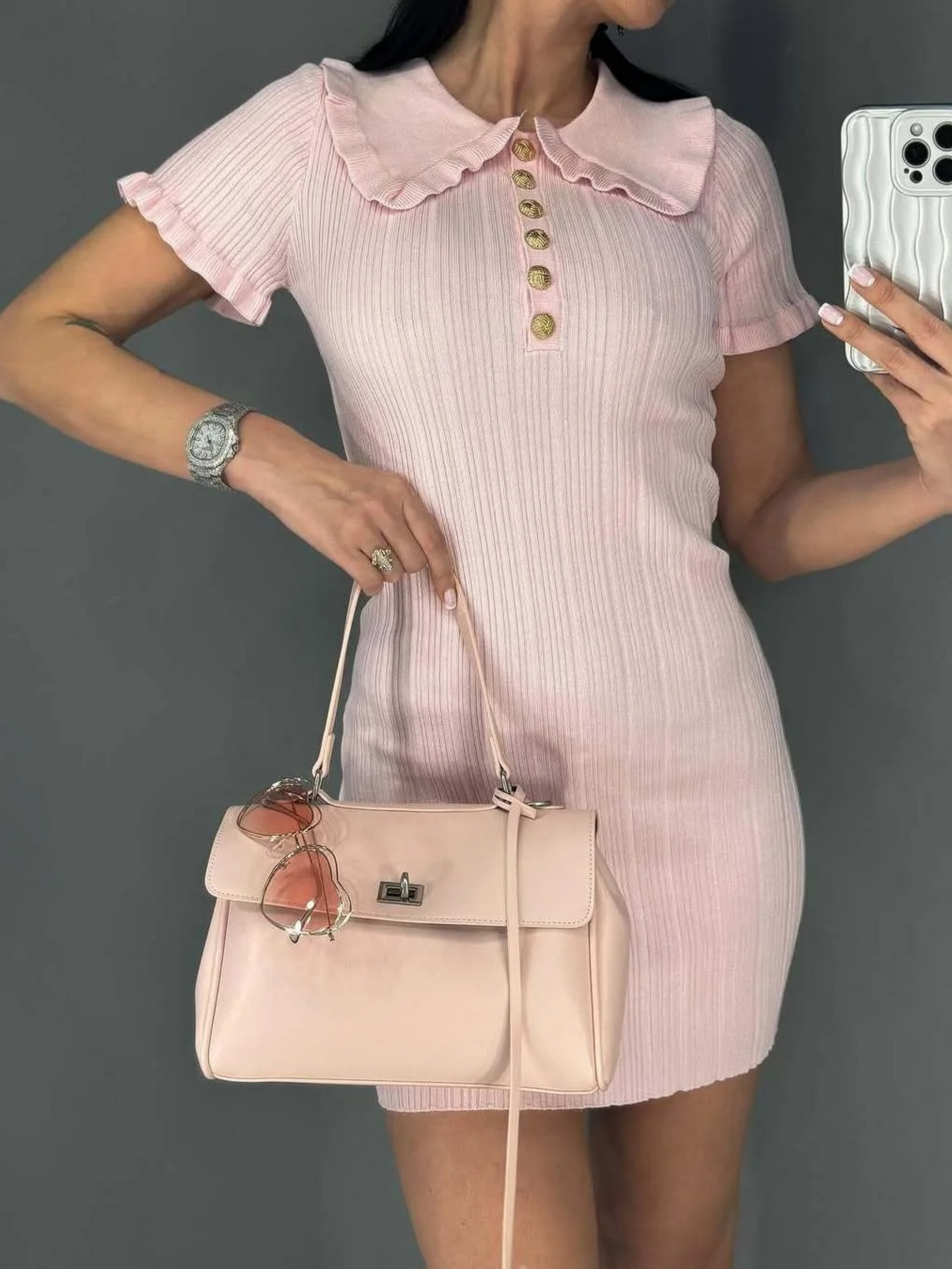 Woman in cream ribbed knit mini dress with ruffle collar and gold buttons sitting at a table.