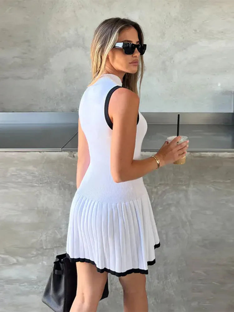 Woman in black ribbed knit mini dress with tan trim, holding coffee and purse.