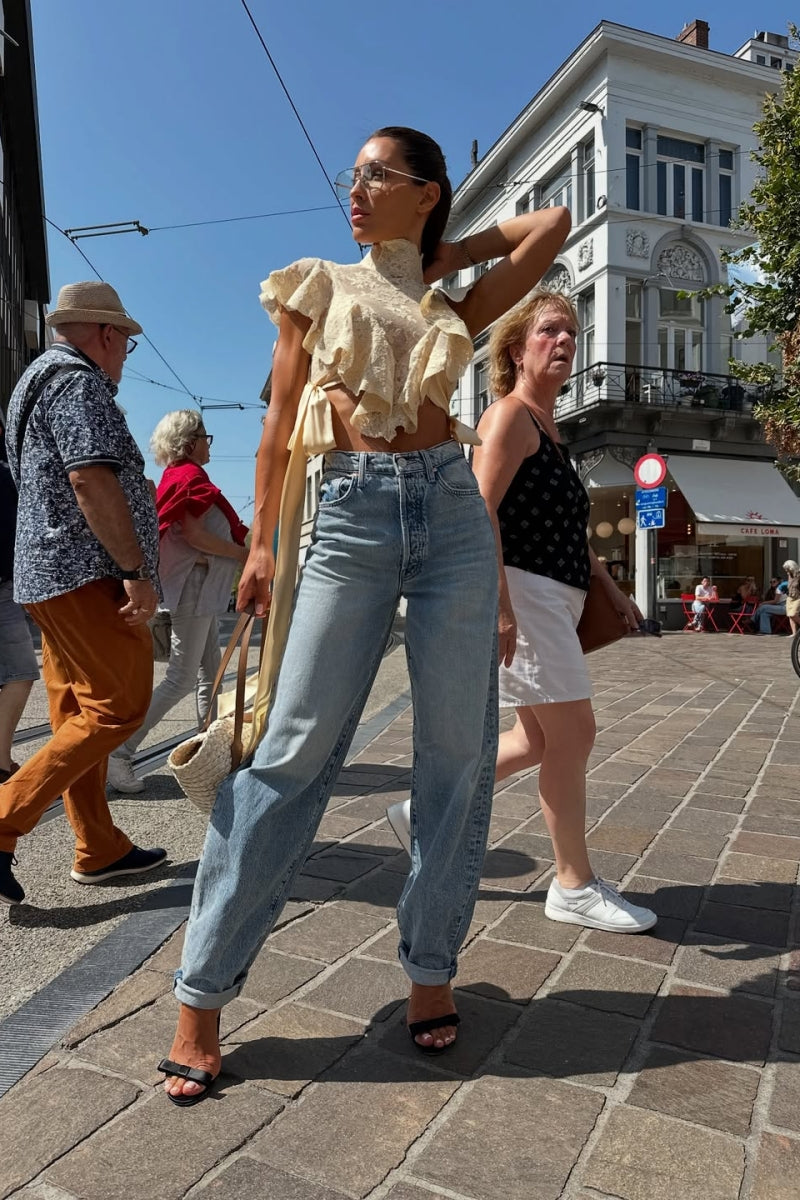 Woman in cream lace crop top and jeans on city street