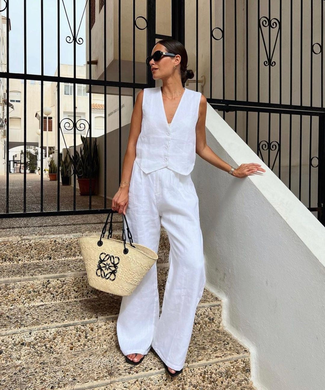 Woman in white linen vest and wide-leg pants on stone steps.