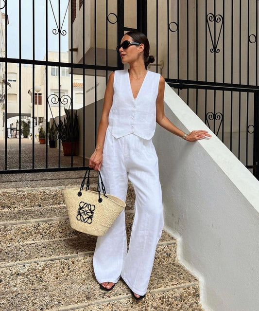 Woman in white linen vest and wide-leg pants on stone steps.