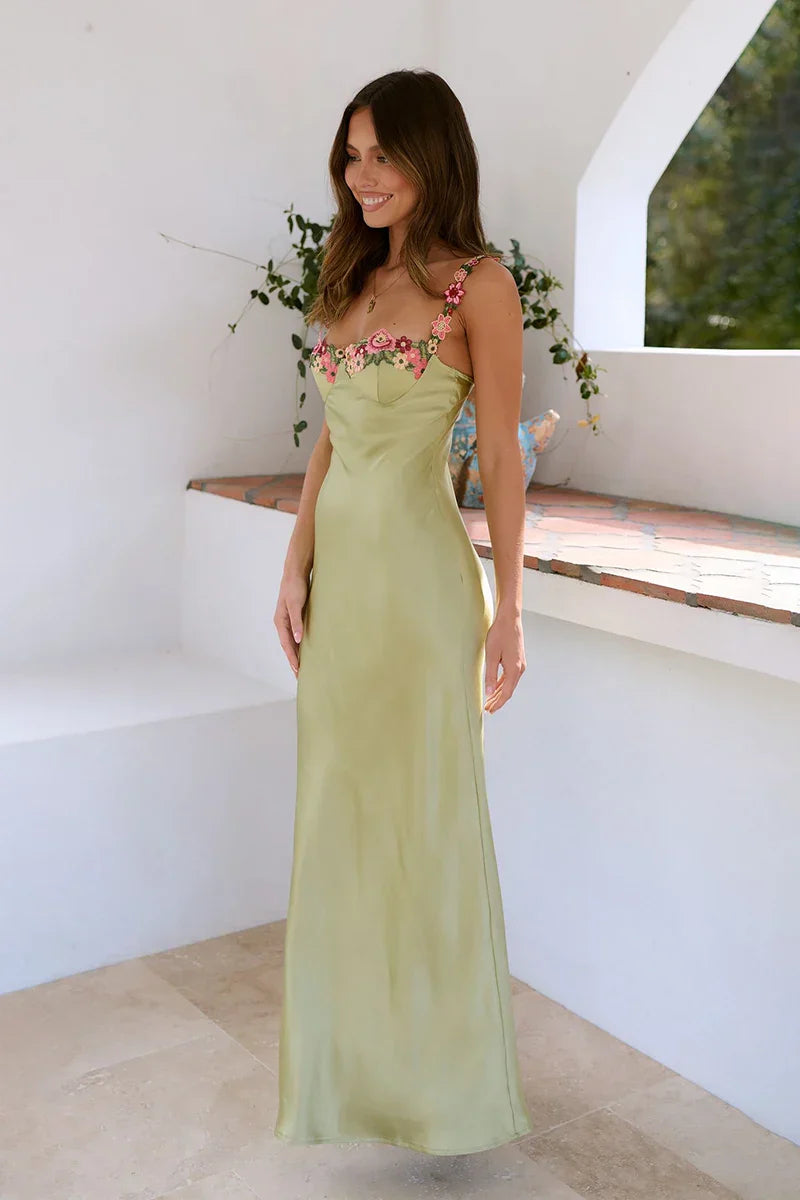 Woman wearing a long pistachio green satin slip dress with floral straps and bodice.