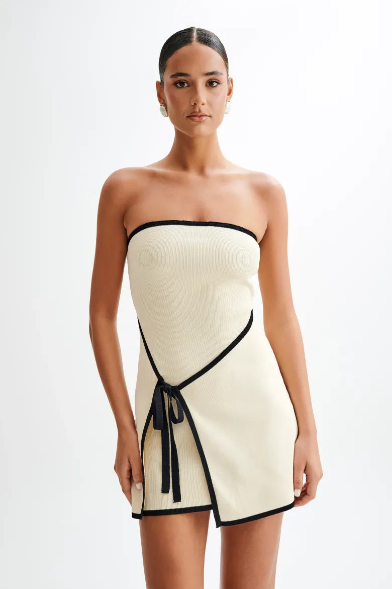 Woman wearing ivory ribbed knit strapless mini dress with black trim and tie waist.
