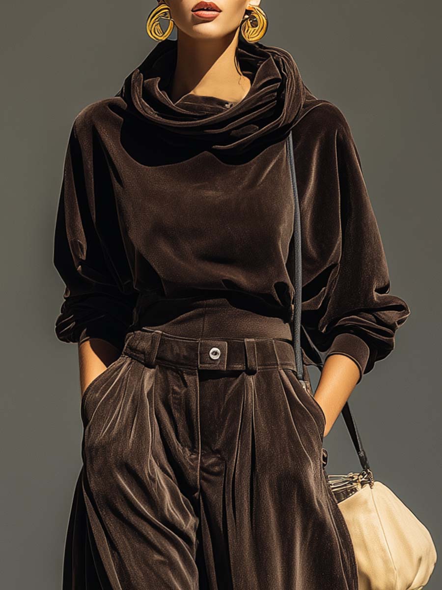 Woman wearing brown velvet cowl neck top and wide leg pants with cream-colored purse.