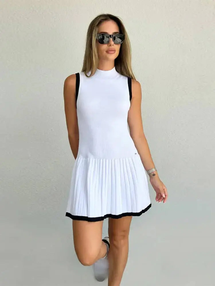 Woman in black ribbed knit mini dress with tan trim, holding coffee and purse.