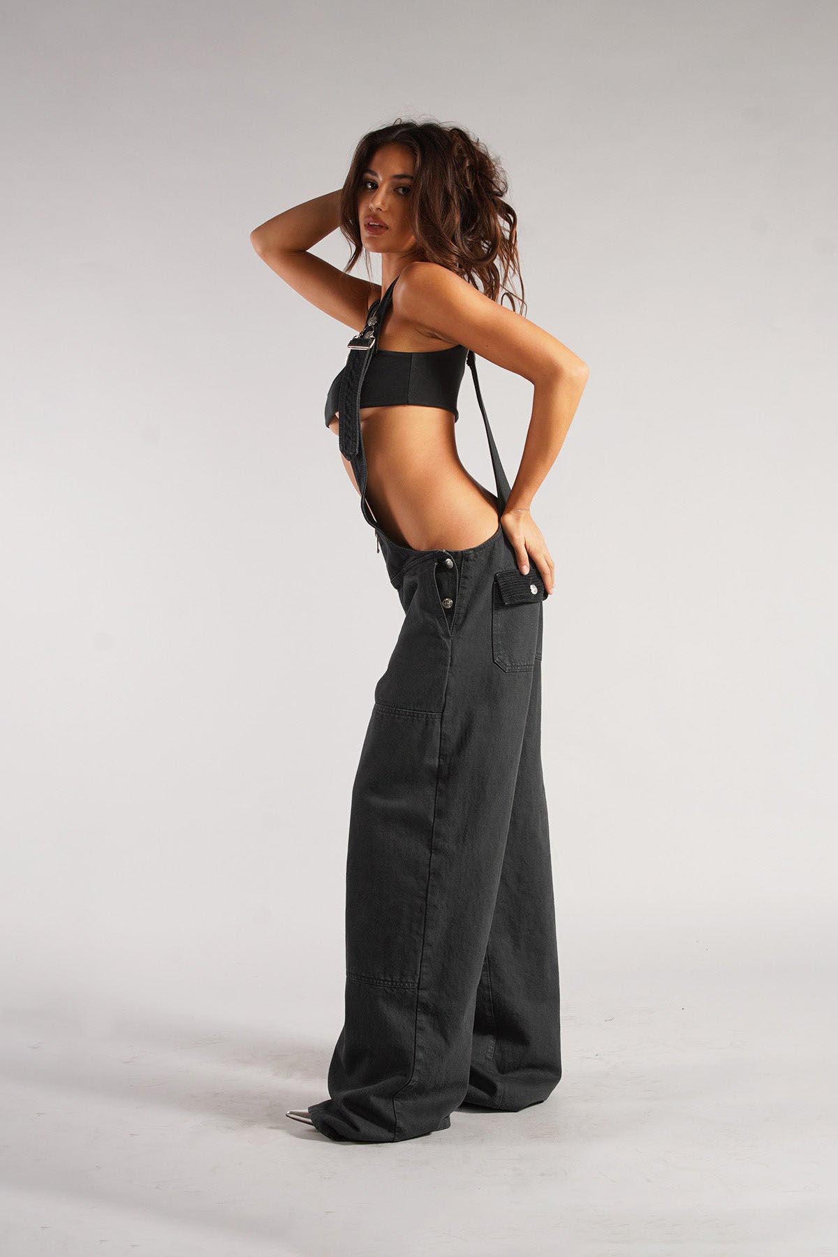 Woman wearing olive green cotton canvas overalls with cutout sides and white crop top