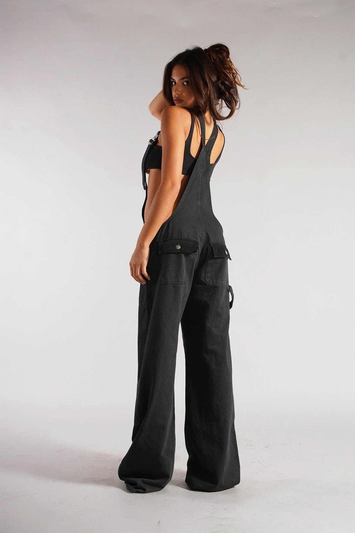 Woman wearing olive green cotton canvas overalls with cutout sides and white crop top