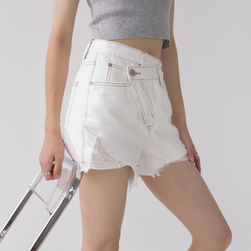 Woman wearing light wash denim shorts with asymmetrical waist and distressed hem.