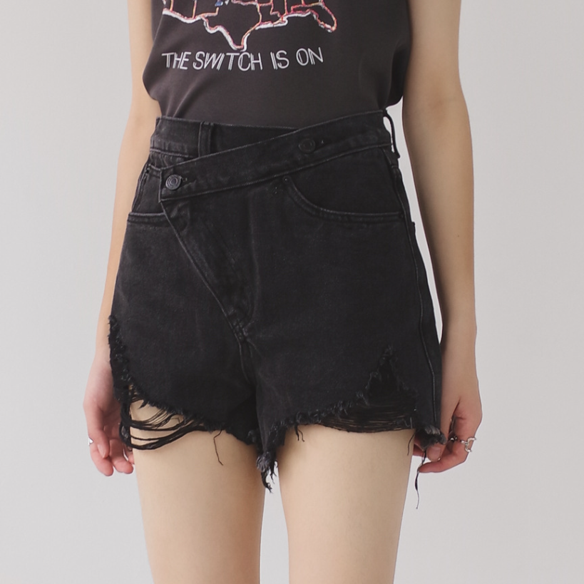 Woman wearing light wash denim shorts with asymmetrical waist and distressed hem.