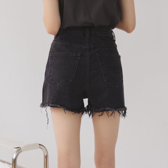 Woman wearing light wash denim shorts with asymmetrical waist and distressed hem.