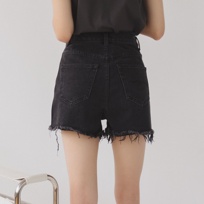 Woman wearing light wash denim shorts with asymmetrical waist and distressed hem.
