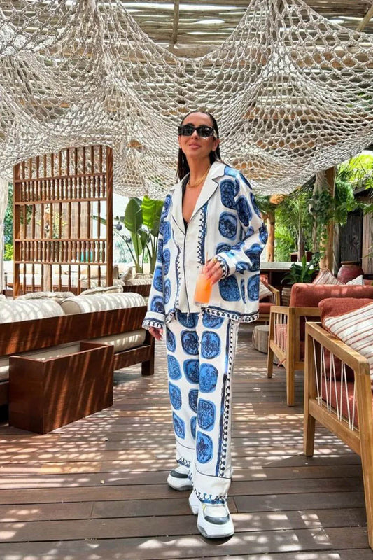 Woman in blue and white printed pajama set with sunglasses and drink.