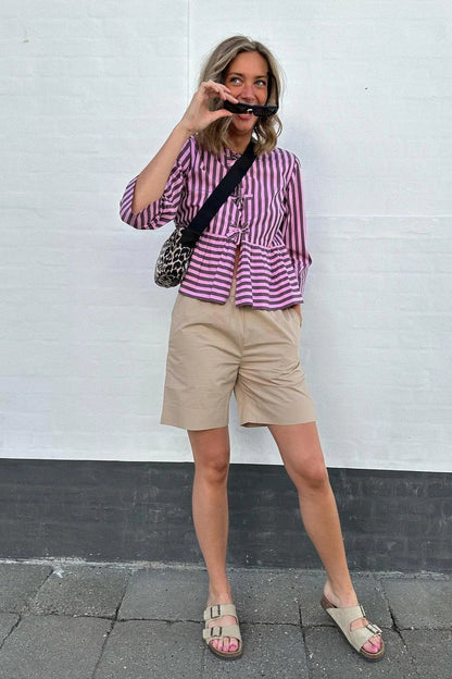 Woman in pink and brown striped blouse and khaki shorts holding sunglasses